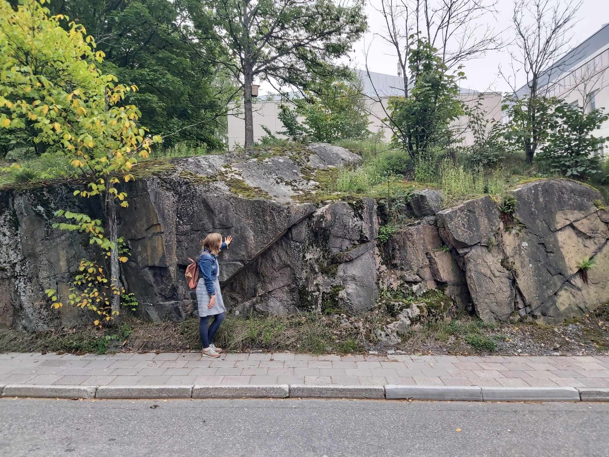 Ett berg vid en väg och en kvinna som står och lutar sig mot det.