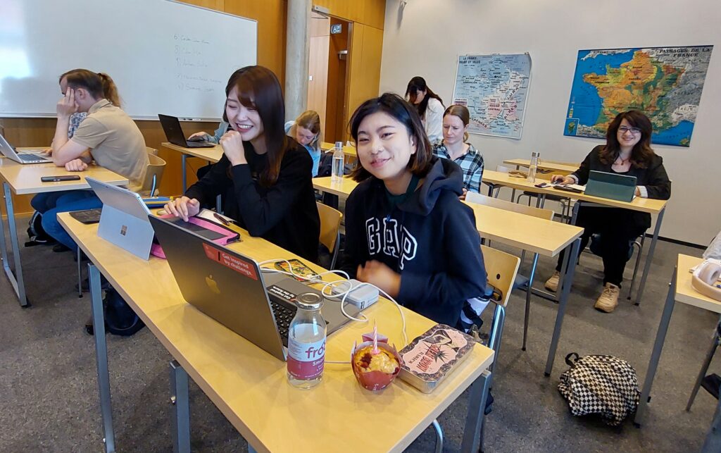 Två leende studerande vid sina datorer.