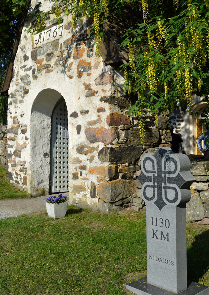 En kyrkport i gråsten, bredvid den en sten med texten 1130 km.