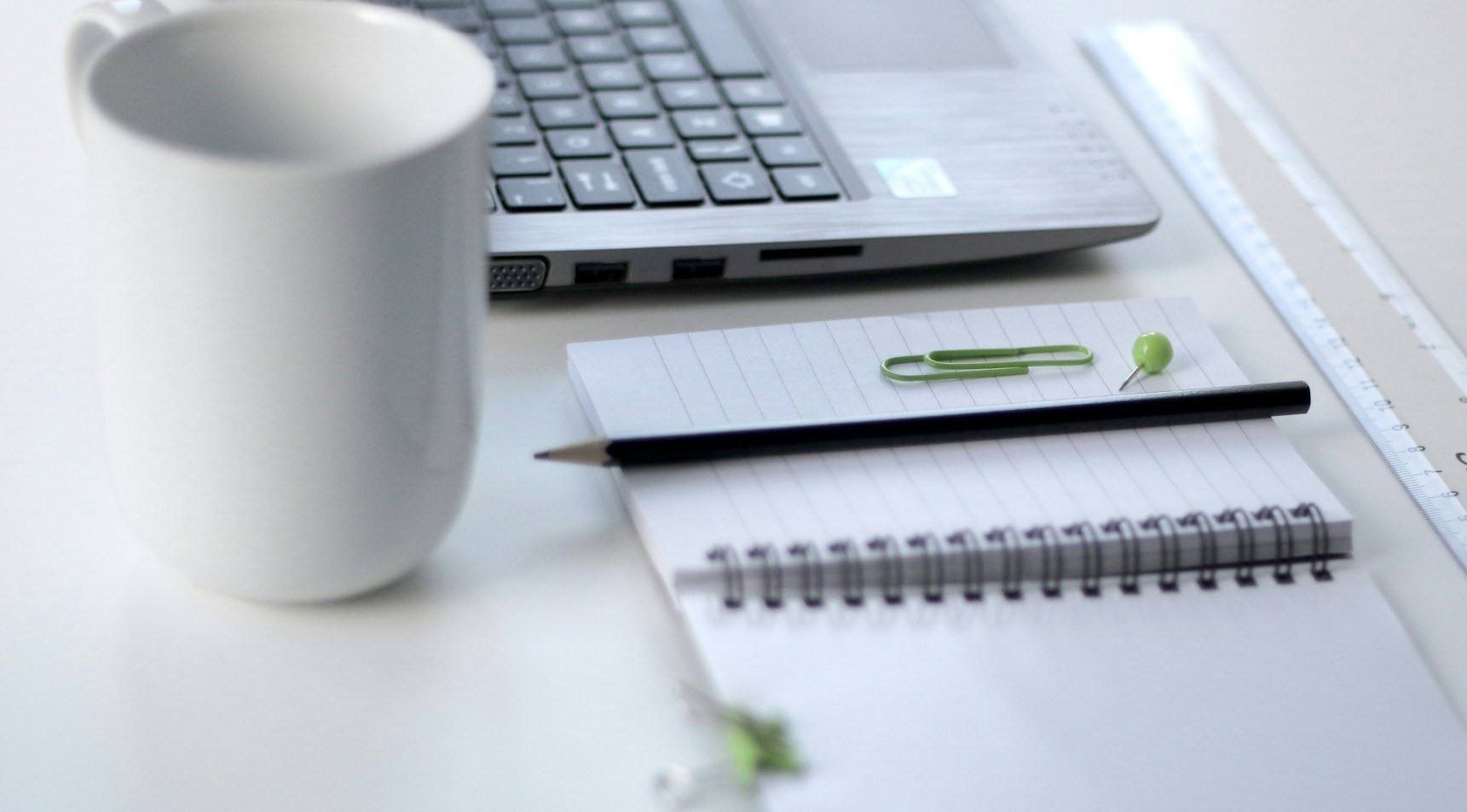 Vit kaffekopp, dator och ett antekcingsblock.