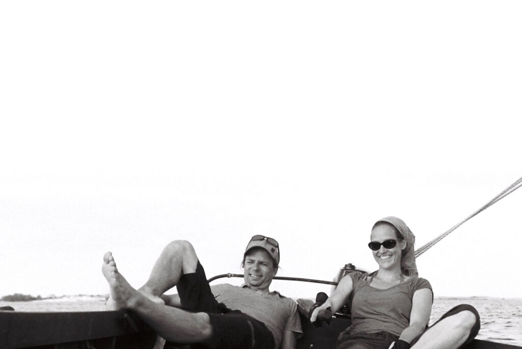 En svart-vit bild på Joel Simberg och Katja Bonnevier, som lutar sig tillbaka mot båtsuden. 