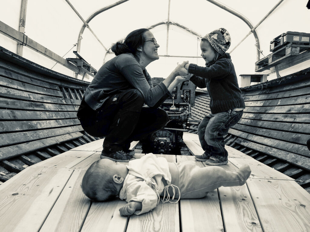 En svart-vit bild där Katja Bonnevier dansar med sin dotter på ett bätdäck, den yngre dottern, en bebis, ligger på däcket.