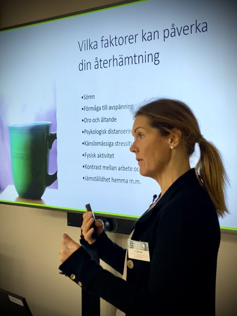 Eva Åstrand fotograferad när hon föreläser om temat Lärarledarskap och står framför en projektorduk med powerpointpresentationen "Vilka faktorer kan påverka din återhämtning".