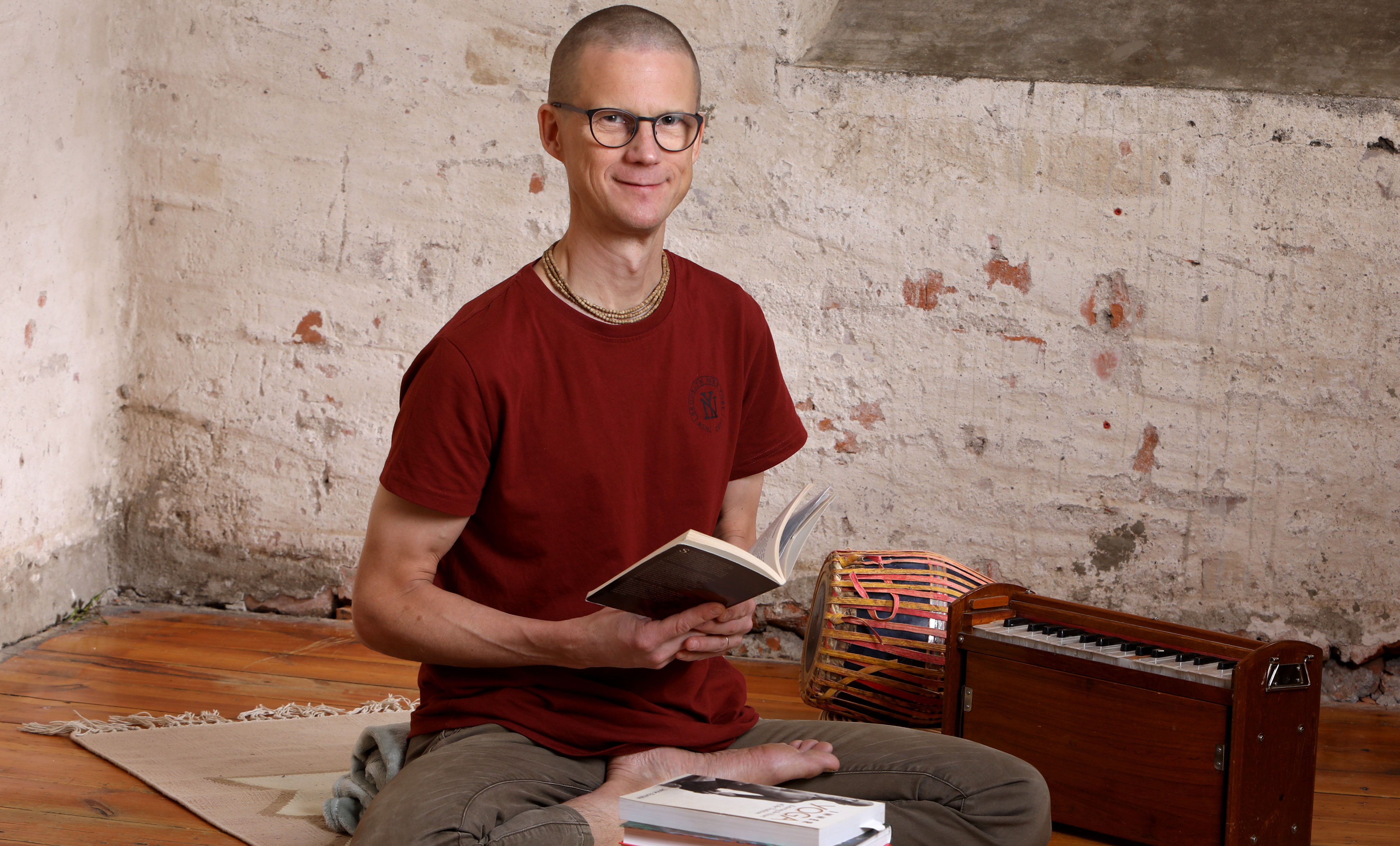 Janne Kontala sitter i yogaställning med en bok i handen och böcker framför sig på en yogamatta.