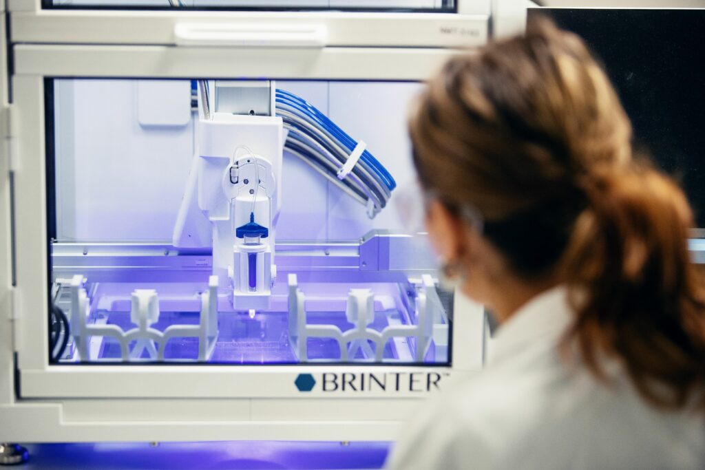 Kvinna i vit rock jobbar med en printer i laboratorium