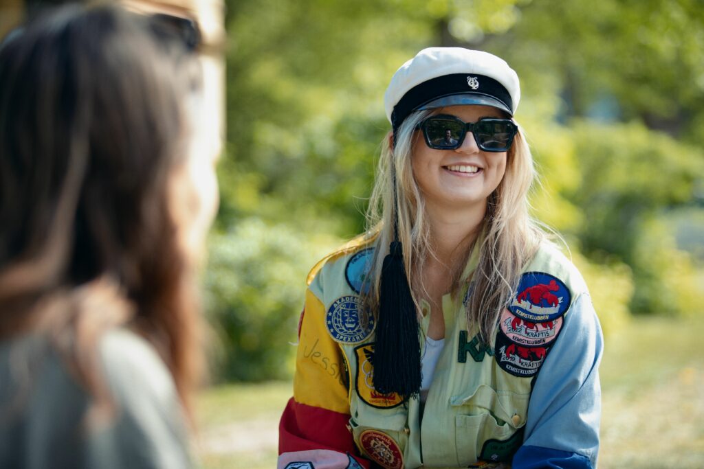 En glad kvinna med blont hår och grön halare som sitter utomhus i en park