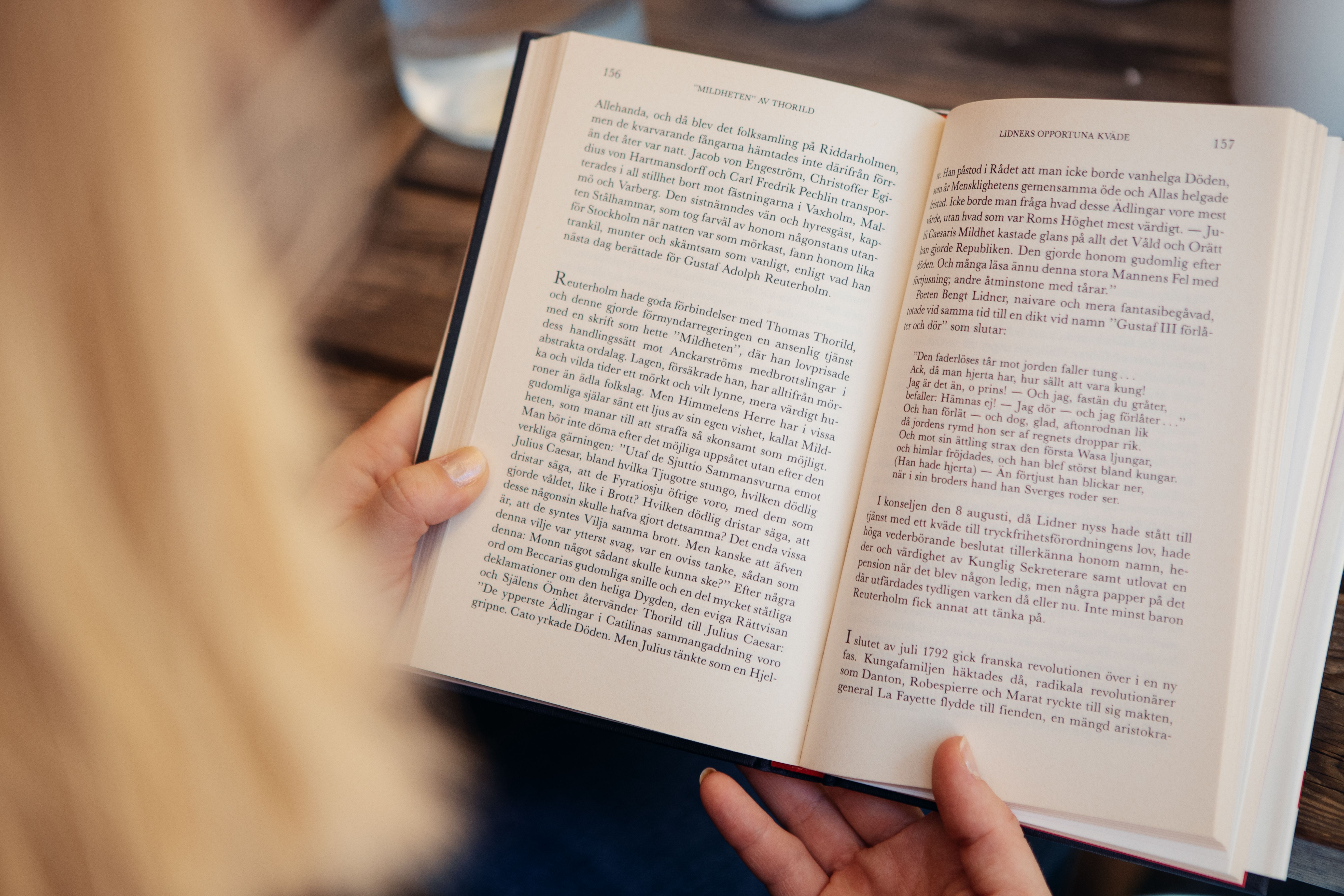 Närbild av blond kvinna som läser en bok i ett café