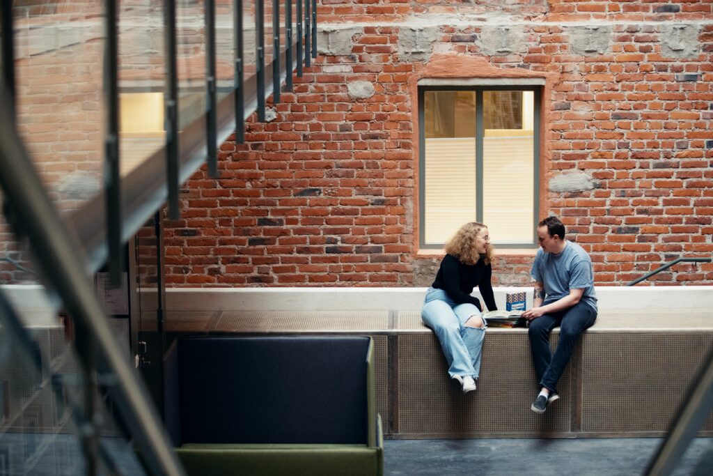 Två studerande sitter på ett bord och tittar på varandra, en av dem håller en bok i handen
