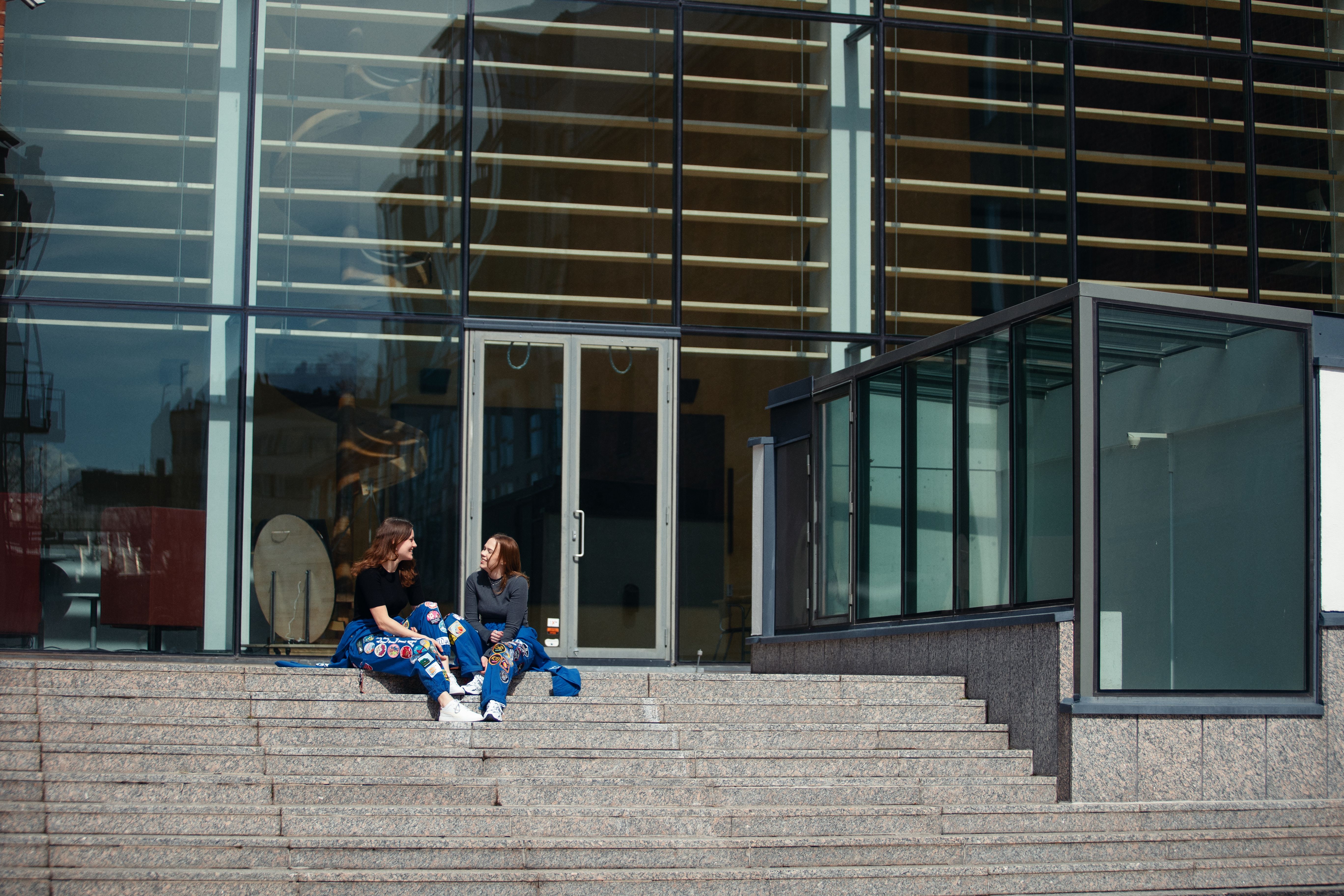 Två studerande i blå halare sitter utanför en universitetsbyggnad