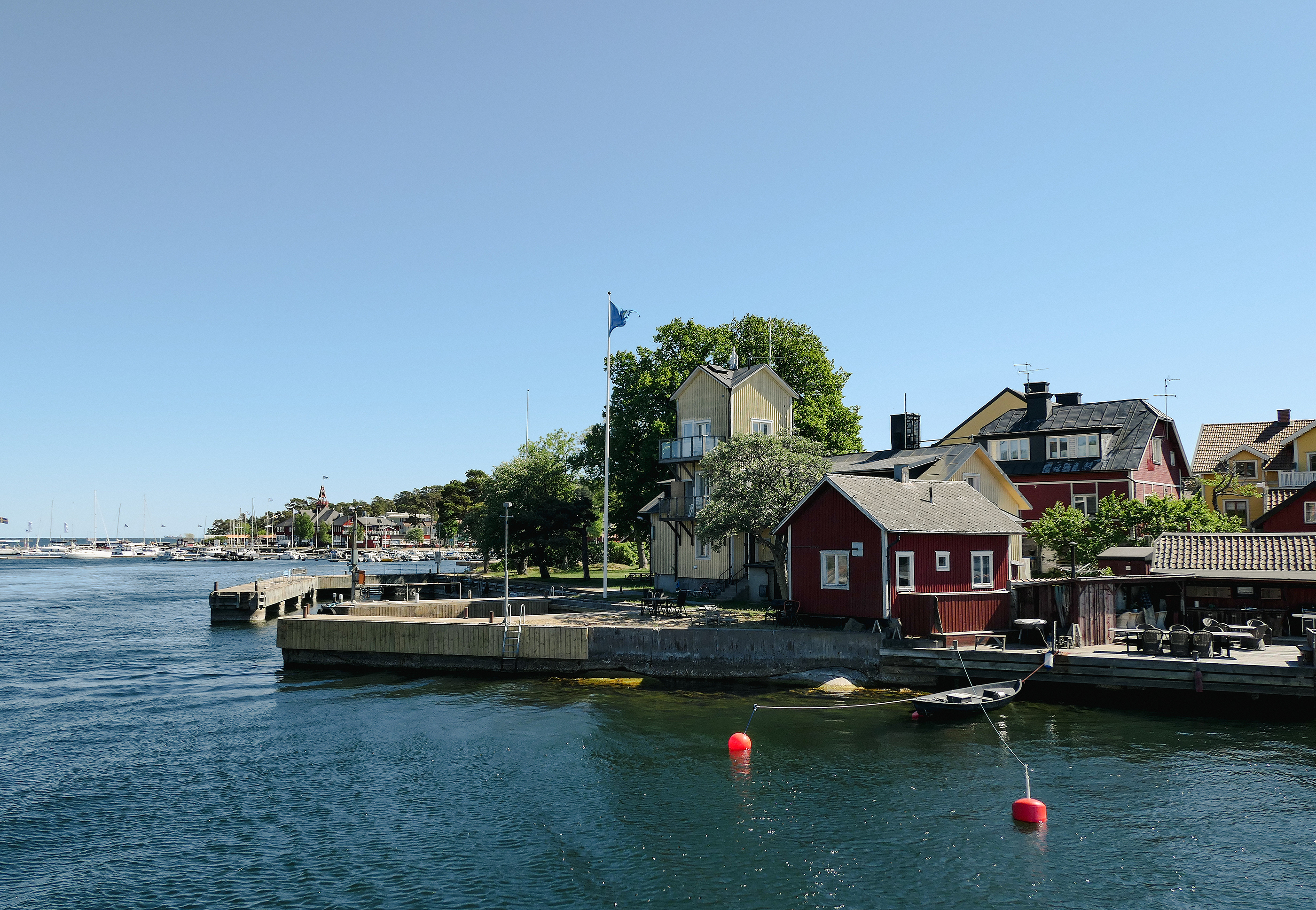 En vy över en strand med röda och gula hus, bilden tagen från vattnet.