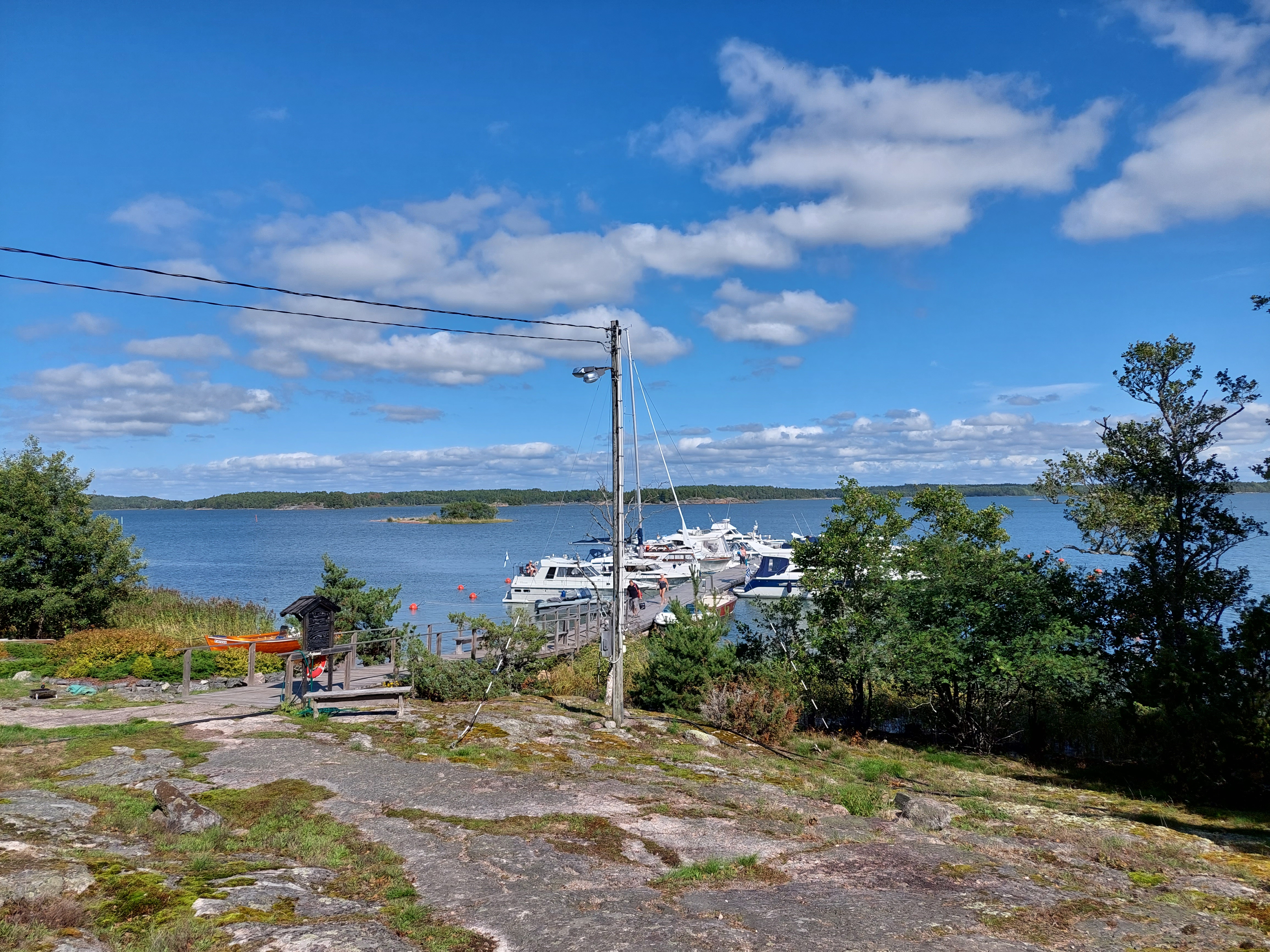 En solig vy över ett berg och en gästhamnsbrygga med båtar.