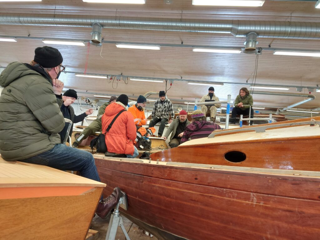 Folk sitter samlade på träbåtar i en hall.