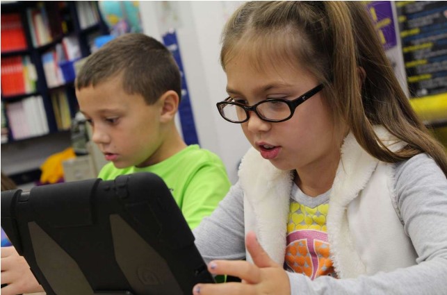 Två barn sitter med varsin läsplatta i händerna