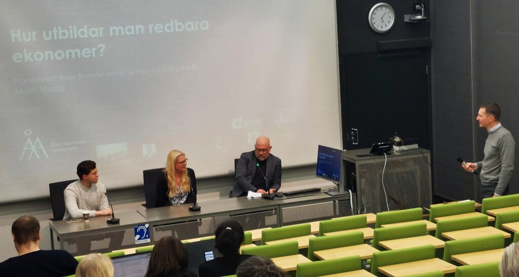 Tre personer bakom en kateder, diskuterar i en panel.