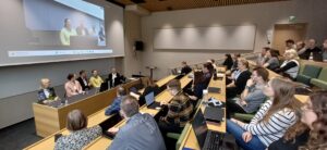 Deltagare och panelister i föreläsningssal.