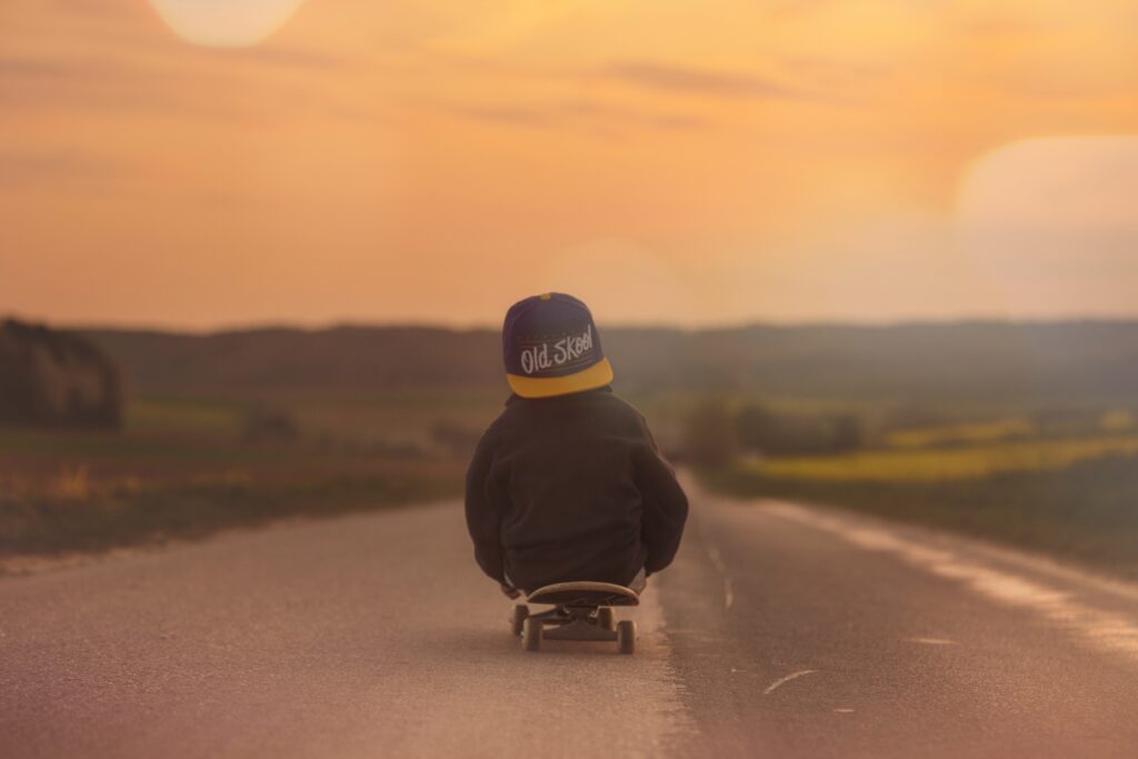 En pojke på en skatebord, åker på en väg i solnedgången