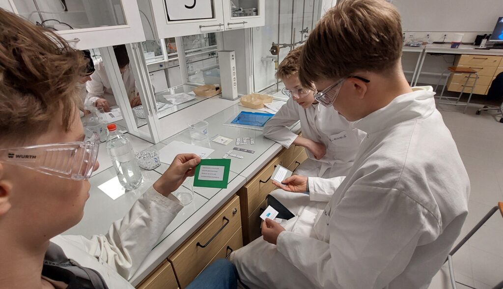 Tre högstadieelever i labbrockar i ett laboratorium.